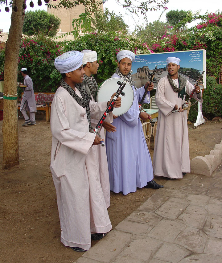 A figura mostra um grupo de músicos vestindo roupas longas e folgadas de cores claras que descem até os pés.