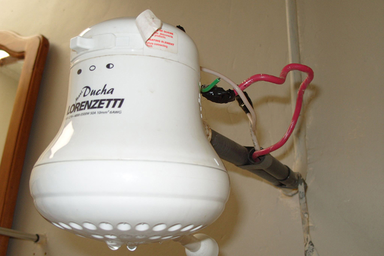 Fotografia de um aquecedor elétrico de água quente conectado ao abastecimento elétrico e de água