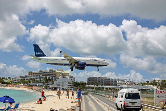 Um avião voando muito baixo até o solo, logo acima de uma praia cheia de espectadores, quando chega para pousar.