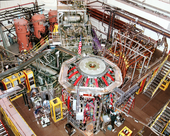 Esta foto muestra el exterior del reactor de fusión del Experimento Nacional de Toros Esféricos en el Laboratorio de Física de Plasma de Princeton. El reactor, que se encuentra en una habitación grande, está conectado a numerosos tubos e instrumentos.