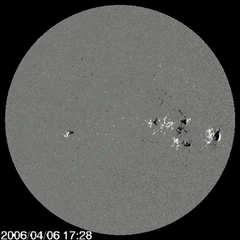 太阳的磁图，在黑色背景下以灰色圆盘的形式出现，上面散布着白色和黑色的斑点。 大多数斑点集中在图像的右中部。