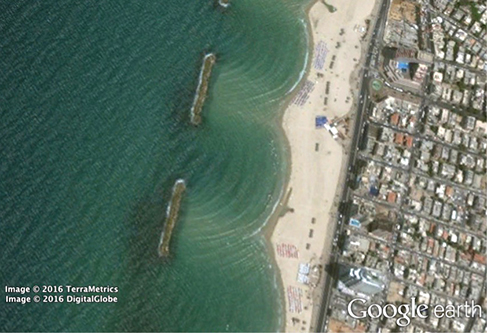 Photographie montrant la vue de dessus d'un brise-lames près d'une plage. Il y a une ouverture dans le brise-lames qui permet aux vagues d'entrer.