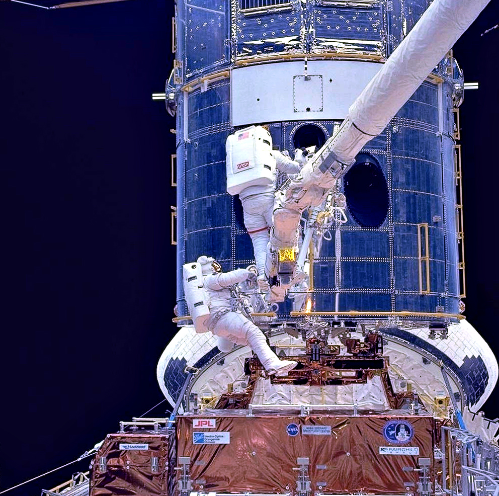 Two astronauts are shown while working on the HST while in space.