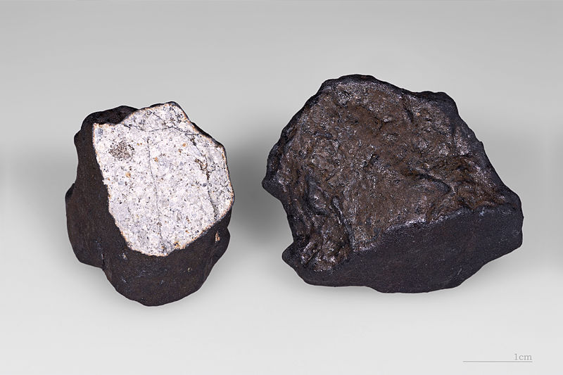 Two meteorites are show, the one on the left has been sliced to show the light color that lies beneath the dark crust.