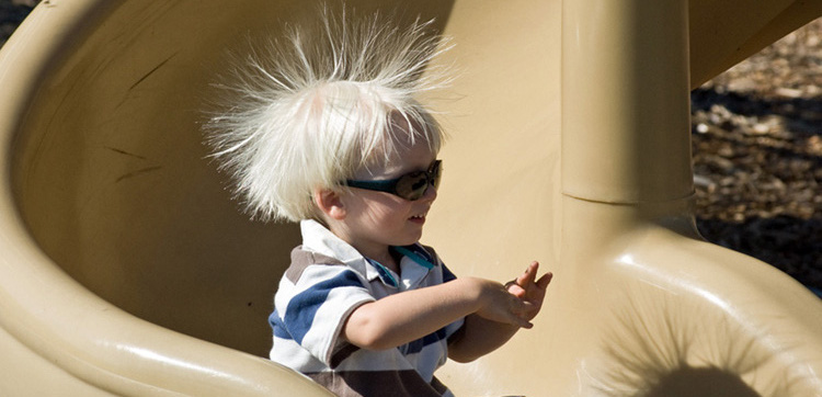 Uma criança desce por um tobogã de plástico, com o cabelo em pé.