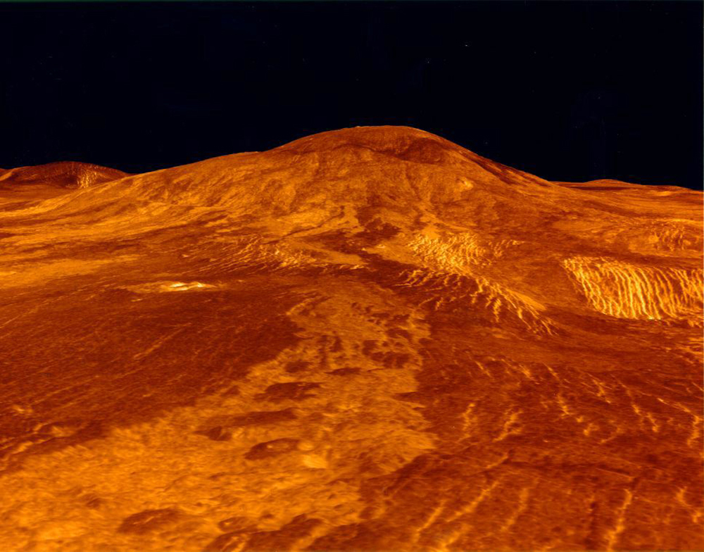 Uma fotografia da superfície do planeta Vênus é mostrada. Os fluxos de lava em Vênus são mostrados como a cor vermelha alaranjada da superfície.