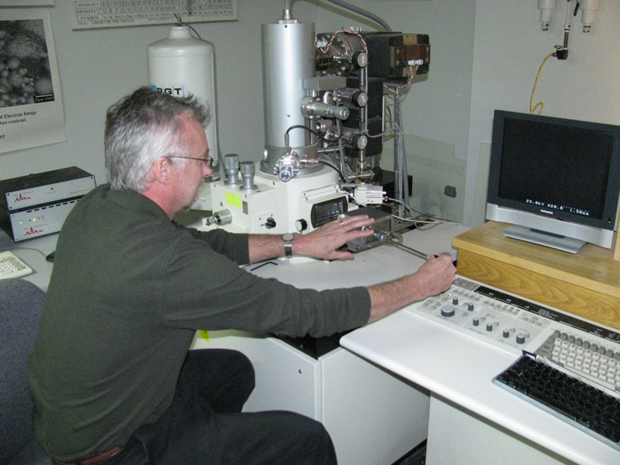 A imagem mostra um homem usando microscópio eletrônico de varredura.
