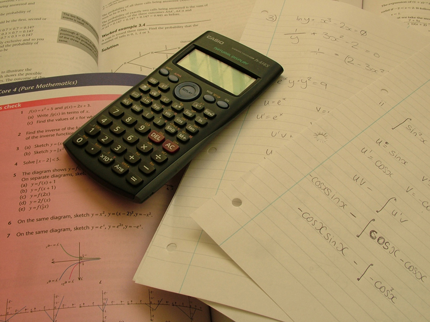 Uma calculadora é colocada em livros de matemática abertos e em alguns papéis. Problemas na trigonometria são resolvidos em um dos artigos.