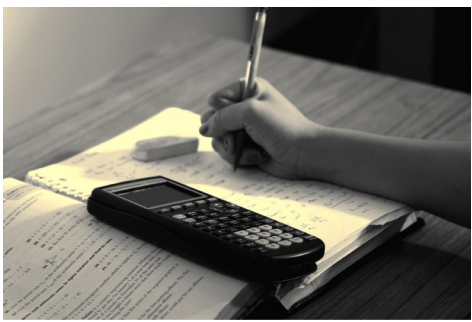 Photographie de la main d'un étudiant travaillant sur un problème à l'aide d'un manuel ouvert, d'une calculatrice et d'une gomme.