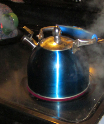 The photograph shows water boiling in a tea kettle kept on a stove. The water vapor is shown to emerge out of the nozzle of the kettle.