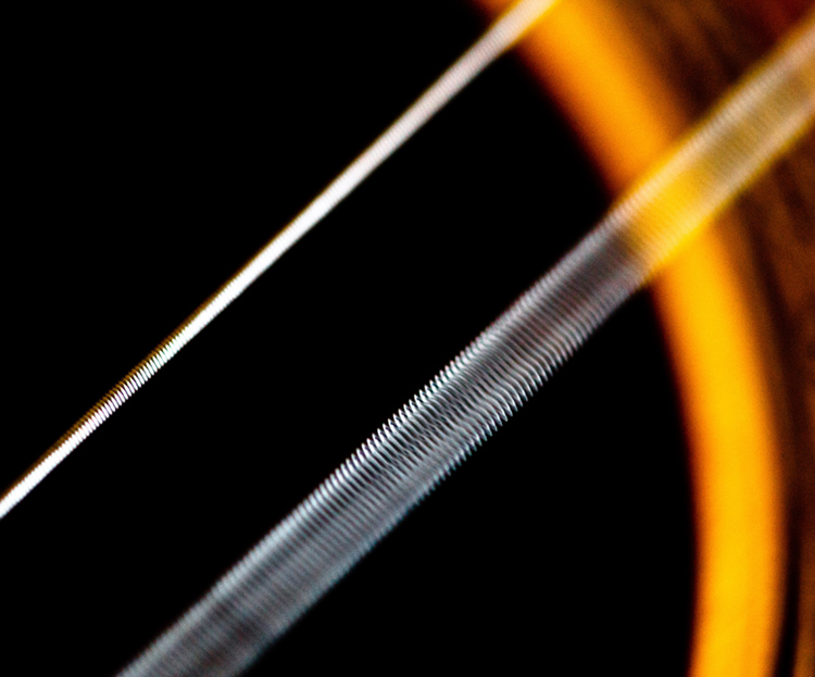 A figura dada mostra uma visão ampliada fechada das cordas de um violão. Há duas cordas brancas inclinadas na imagem. Na corda mais próxima, as lacunas entre as roscas circulares da corda são visíveis, enquanto a segunda corda branca na parte de trás parece uma vara branca fina.