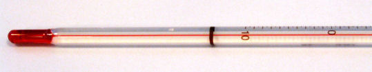 Imagem da extremidade inferior de um termômetro de vidro contendo álcool e um corante vermelho.