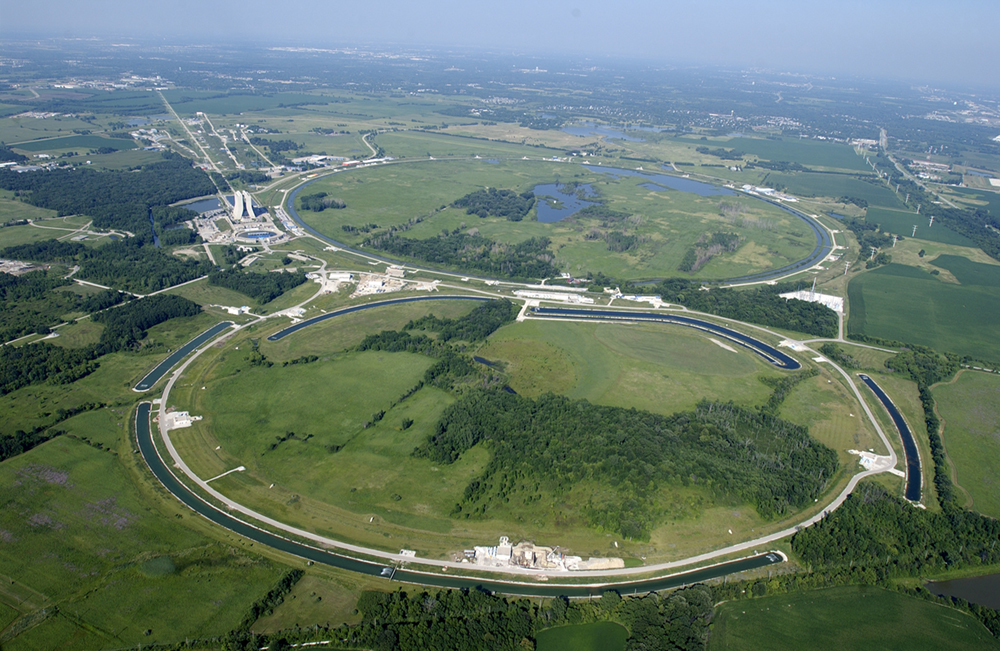 Una vista aérea del Laboratorio Nacional Acelerador Fermi. El acelerador tiene dos grandes estructuras en forma de anillo. Hay estanques circulares cerca de los anillos.