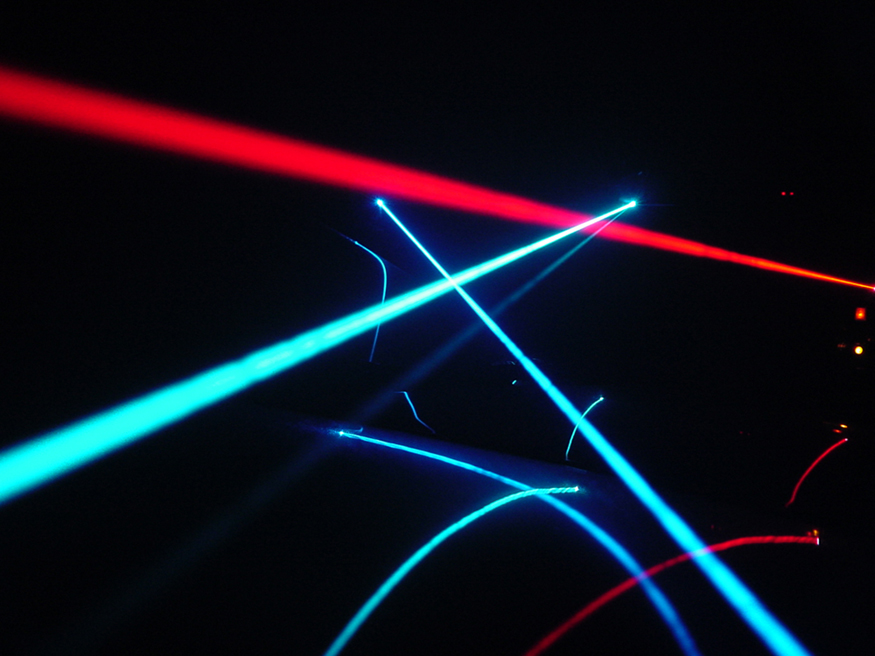 A imagem mostra vários raios laser de cor vermelha e azul que se parecem com holofotes.
