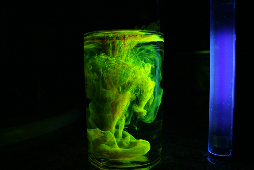 Um copo de água no qual é adicionado pó fluorescente. Perto do copo, uma fonte de luz ultravioleta é colocada. Nessa luz ultravioleta, o pó fluorescente na água brilha como fumaça verde.