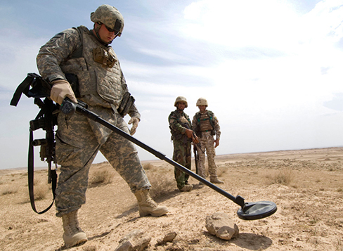 A fotografia mostra um soldado com o detector de metais em uma mão.