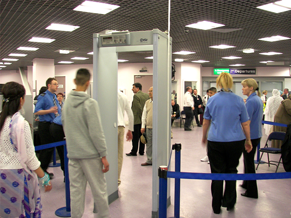 Photographie de personnes faisant la queue devant la porte d'un détecteur de métaux d'un aéroport.