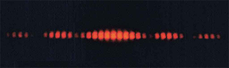 La figure est une image montrant un motif d'interférence rouge sur fond noir. La partie centrale présente des lignes plus claires. Les lignes sont coupées en haut et en bas, apparemment enfermées entre deux ondes sinusoïdales de phase opposée.
