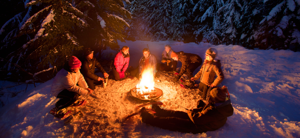 Fotografia de pessoas sentadas ao redor de uma fogueira na neve.