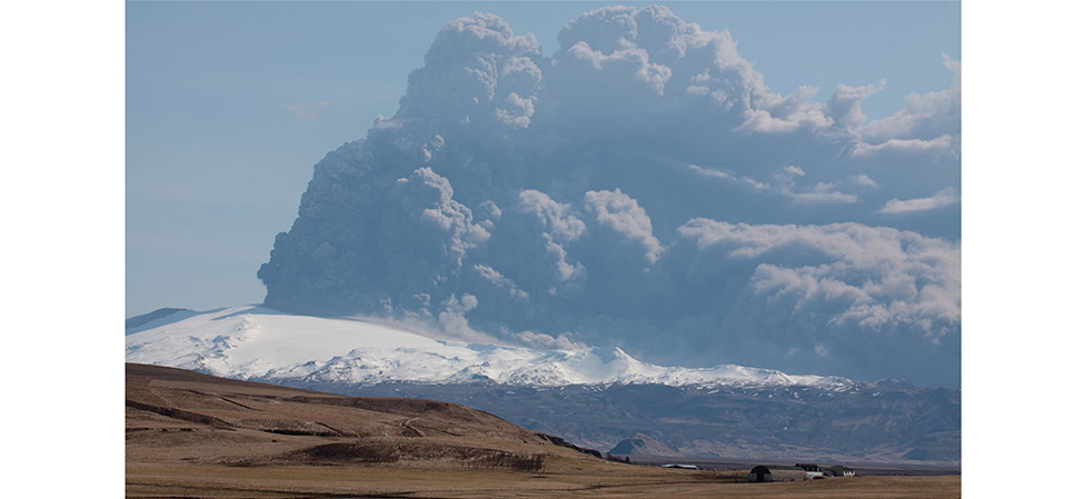 Uma fotografia de um vulcão em erupção. Uma nuvem gigante de gás e poeira pode ser vista sendo ejetada dela.