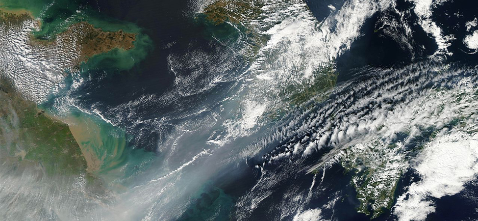 Uma fotografia de satélite do nordeste da China. Nuvens cobrem parte da vista. A parte inferior esquerda da imagem está obscurecida pela poluição.