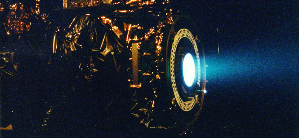 The photo shows a xenon ion engine and a blue glow emitted from it.