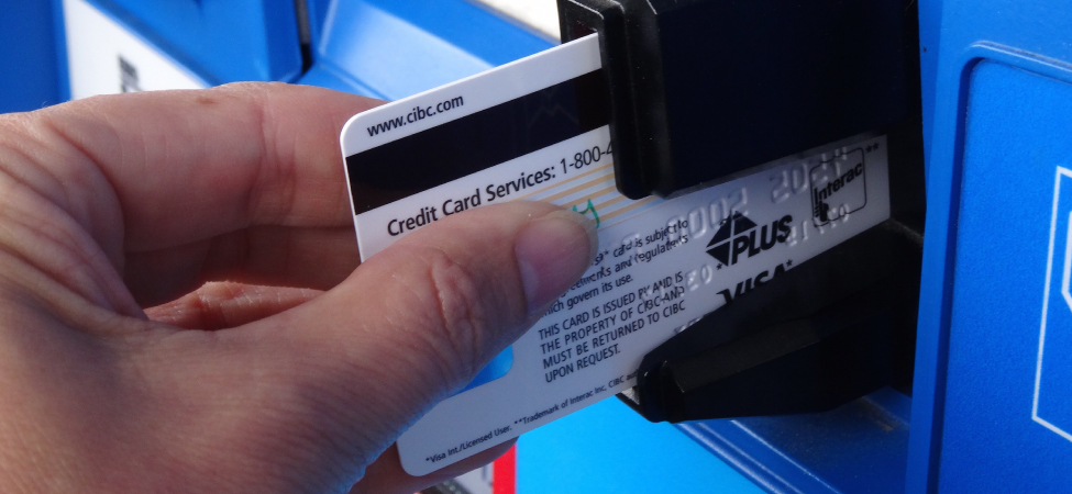La figure est la photo de la carte de crédit insérée à mi-chemin dans la fente du guichet automatique de manière à ce que la bande magnétique noire soit visible.