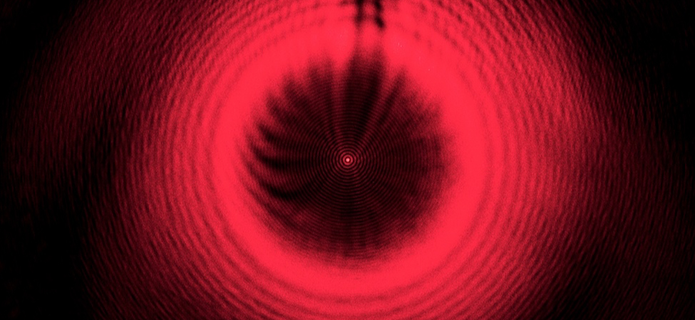 Figure shows a series of red concentric rings on a black background. At the center is a bright red spot.
